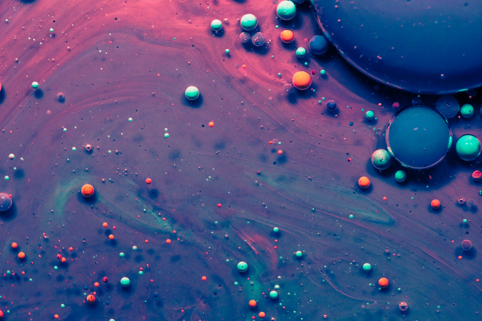 Macro photograph of coloured droplets suspended on a swirling pink and blue liquid surface